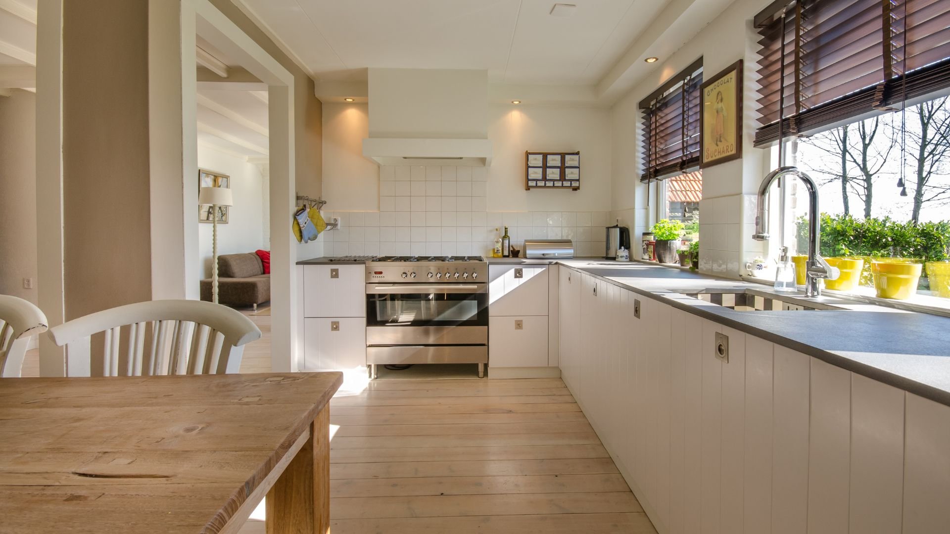 Modern white kitchen with wooden table, stainless steel appliances, and bright window